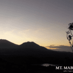 Scenic view of Mt. Mabilog in Laguna, Philippines, during sunrise, with silhouetted peaks, gradient sky, and trees by a small body of water, taken in 2013