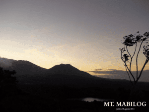 Scenic view of Mt. Mabilog in Laguna, Philippines, during sunrise, with silhouetted peaks, gradient sky, and trees by a small body of water, taken in 2013