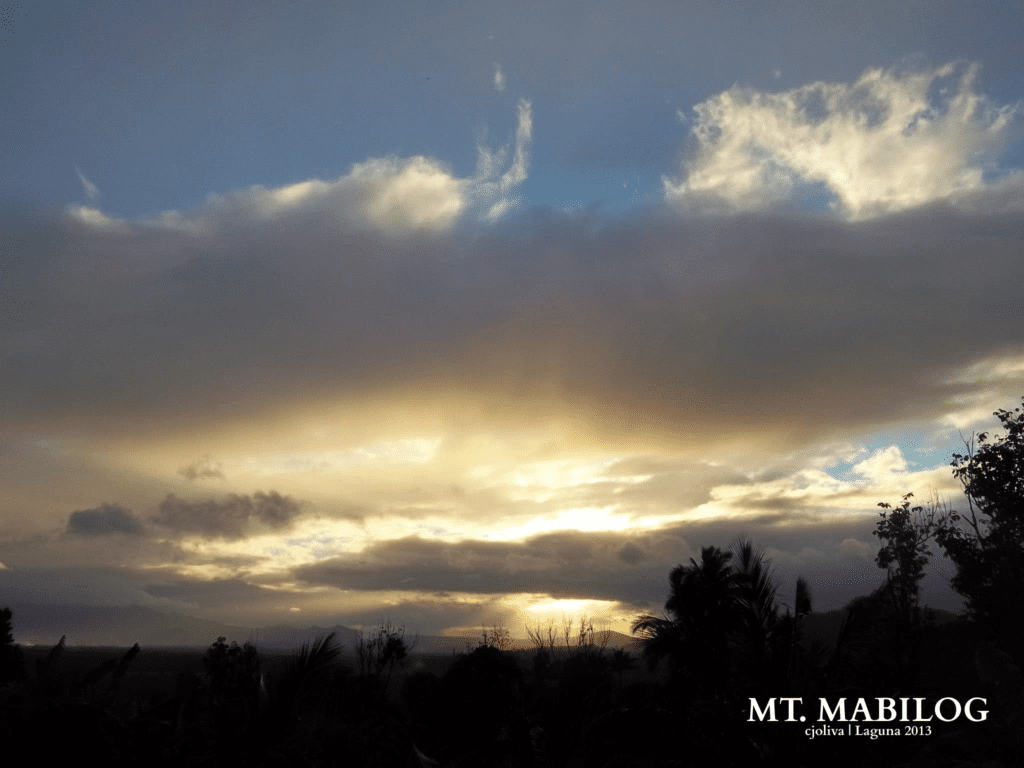 Dramatic sunset with golden light breaking through clouds over Mt. Mabilog in Laguna, with silhouetted trees in the foreground, 2013.