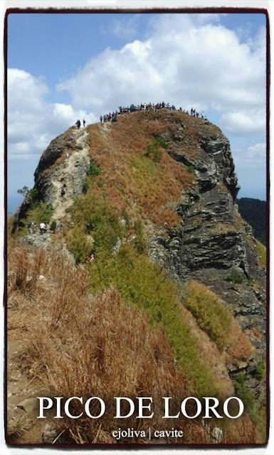 A large group of hikers standing on the rocky summit of Mt. Pico de Loro in Cavite under a cloudy blue sky.