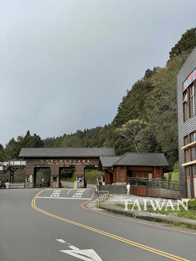 Wooden entrance to Alishan National Forest Recreation Area in Taiwan surrounded by lush green hills with road and pedestrian walkway leading in