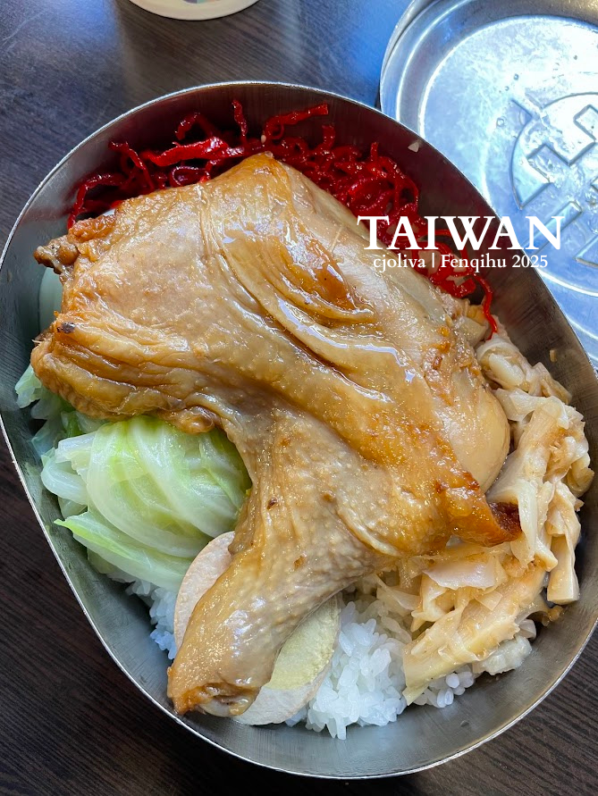 A classic Fenchihu Railway Bento in a metal tin, featuring a large braised chicken leg, cabbage, bamboo shoots, and a braised egg over white rice.