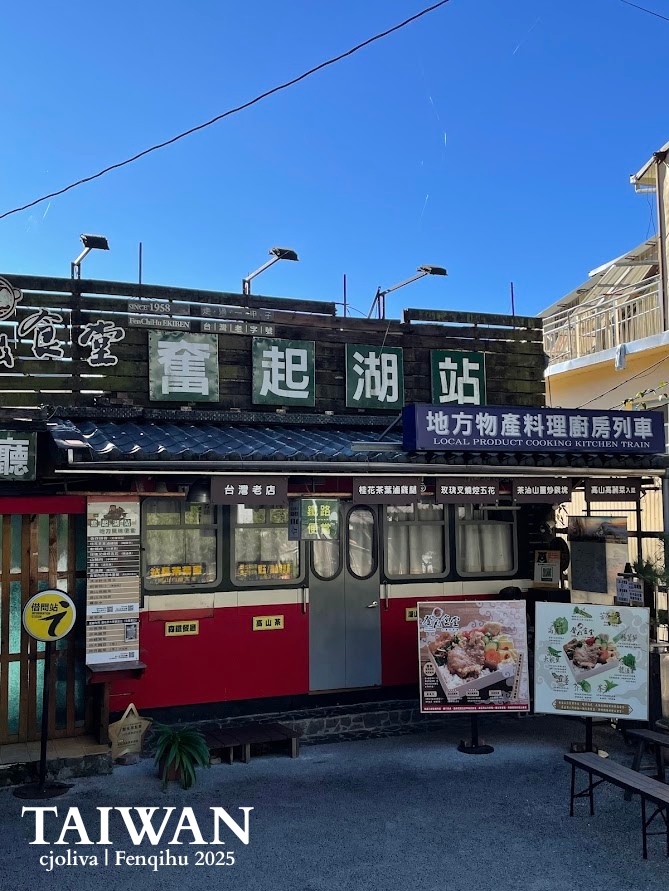 A rustic railway-themed bento shop in Fenqihu, Taiwan, designed to look like a red and white train car, with signs for local specialty lunch boxes under a clear blue sky.