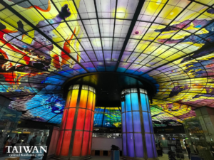 Wide-angle shot of the Dome of Light stained-glass ceiling at Formosa Boulevard Station, Kaohsiung, featuring the iconic blue and red illuminated pillars.