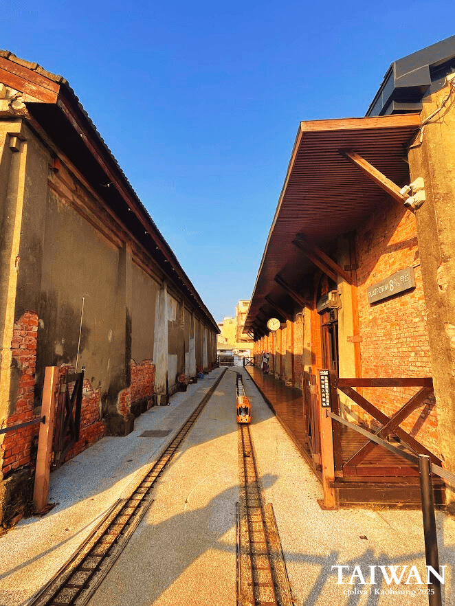 A bright orange miniature train on a small-scale track running between two historic brick warehouses at Hamasen