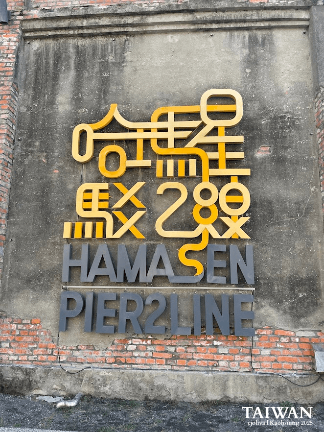 Modern yellow and grey signage for the Hamasen Pier 2 Line on an aged brick wall in Kaohsiung