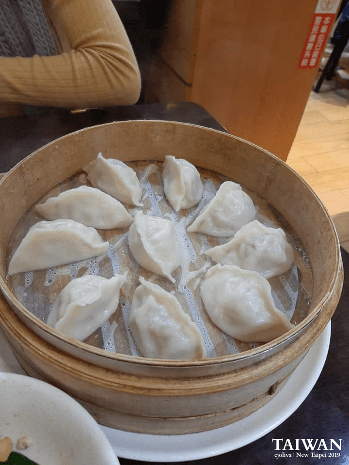 Bamboo steamer basket filled with freshly steamed dumplings on a white plate in a Jiufen restaurant, taken in 2019