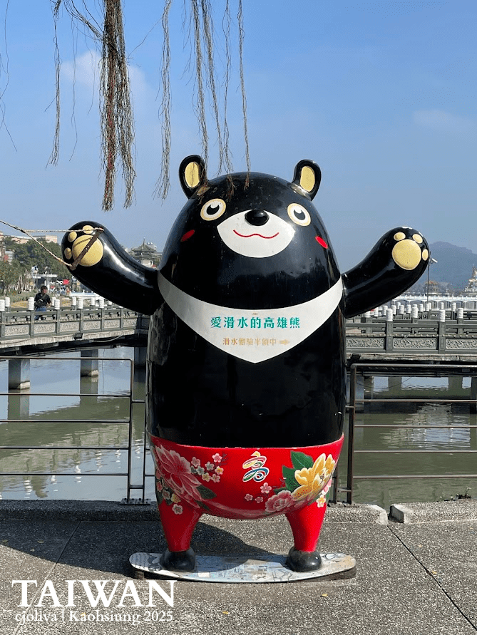 A large, friendly statue of Kao Hero (Kaohsiung Bear) with a "V" on its chest and a heart, standing at a tourist information center in Taiwan.