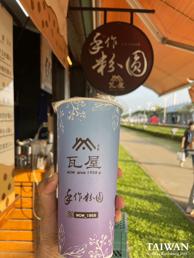 Hand holding a tall purple and blue cup of iced tea from a local street vendor at Pier-2 Art Center in Kaohsiung during the golden hour