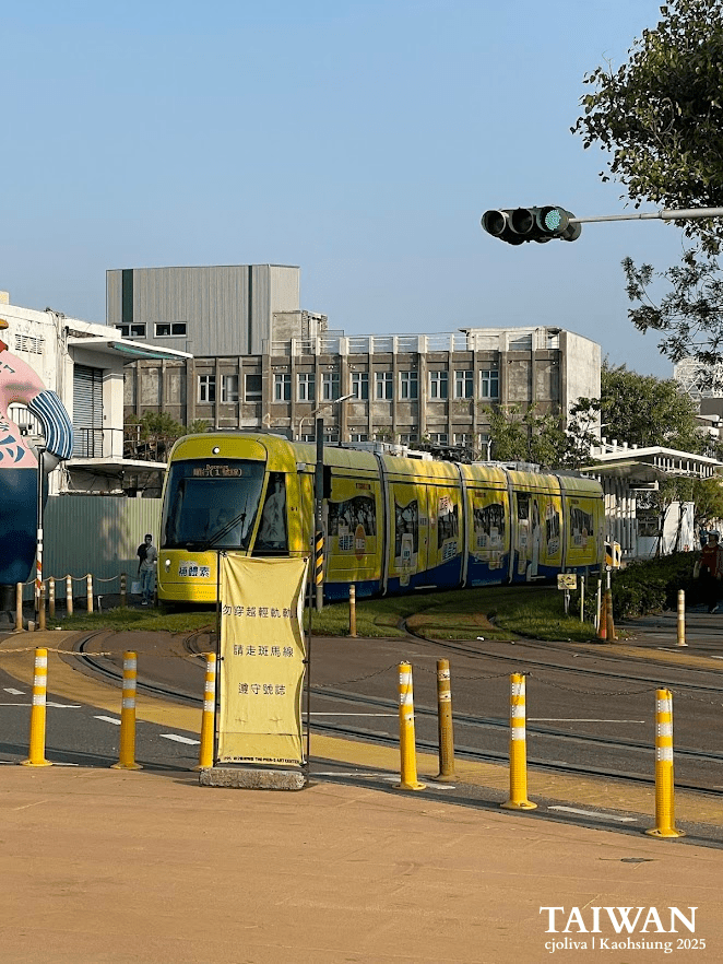 Modern yellow Kaohsiung Light Rail tram turning a corner past a station platform