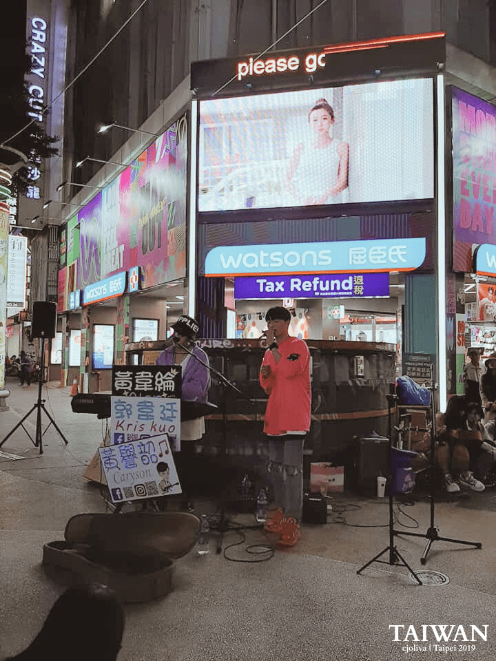 Singer and keyboard player performing in Ximending, Taipei, Taiwan, with promotional sign for Kris Kuo and social media links, in front of Watsons store and digital ads, taken in 2019