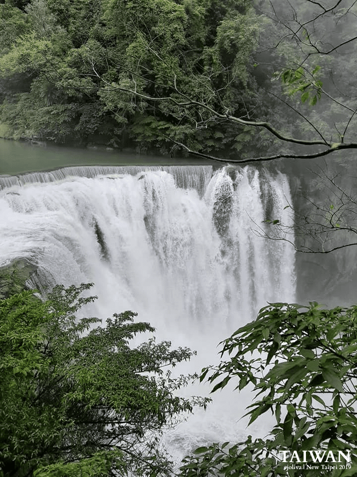 A powerful waterfall cascading over rocky ledge surrounded by lush green forest vegetation in New Taipei, Taiwan, taken in 2019