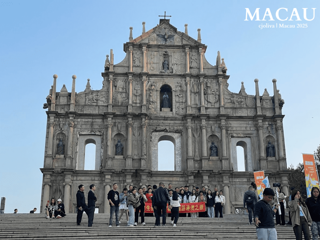 The towering 17th-century stone facade of the Ruins of Saint Paul's with intricate carvings, standing at the top of a wide stone staircase with tourists gathered below.