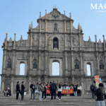 The towering 17th-century stone facade of the Ruins of Saint Paul's with intricate carvings, standing at the top of a wide stone staircase with tourists gathered below.
