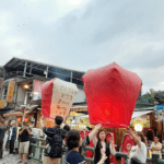 People releasing large red sky lanterns with handwritten messages along Shifen Old Street railway track in New Taipei, Taiwan, with airborne lanterns in the background, taken in 2019