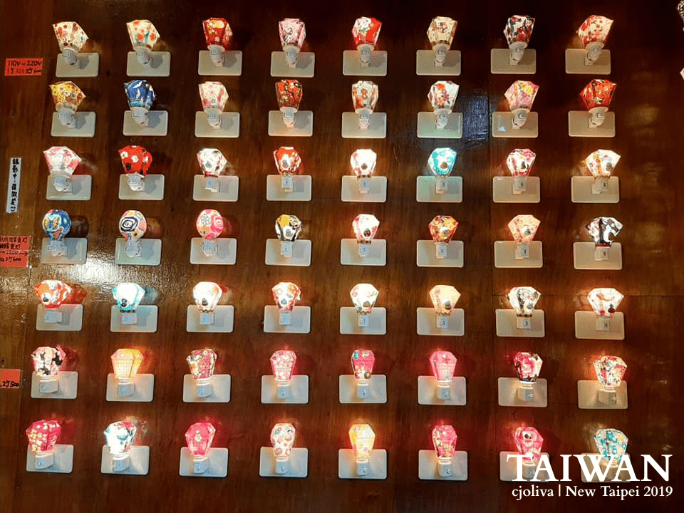 Grid display of colorful lantern-shaped souvenir night lights arranged on a wooden wall in a shop near Shifen Waterfalls, New Taipei, Taiwan, taken in 2019