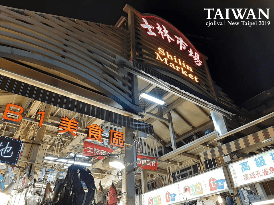 Illuminated entrance to Shilin Market in Taipei, Taiwan, at night, with signage in Chinese and English, modern architecture, and bustling shops, taken in 2019