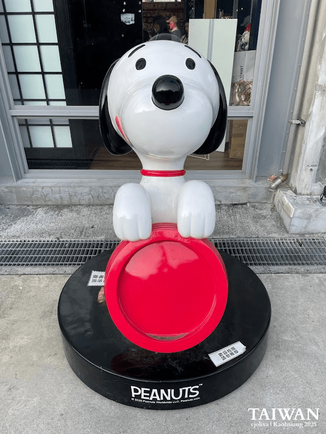 Large Snoopy statue holding a red bowl on a black "Peanuts" base outside a shop at Pier-2 Art Center in Kaohsiung.