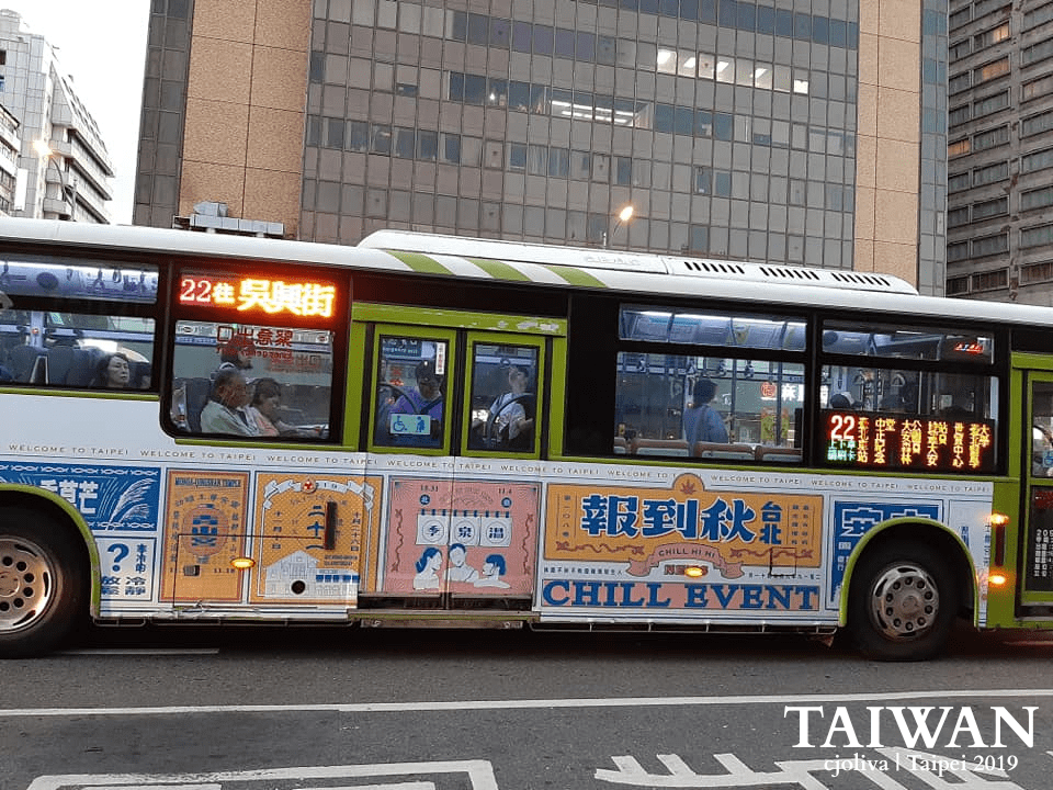 A Taipei city bus with colorful advertisements and a route display for Wu Xing Street.