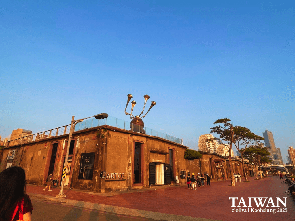 Old brick warehouse building with an ARTCO sign and a large trumpet-like rooftop sculpture at the Pier-2 Art Center in Kaohsiung during sunset