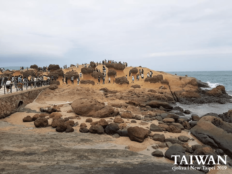 Mushroom-shaped sandstone rock formations at Yehliu Geopark in New Taipei, Taiwan, with visitors exploring paths along the rocky coast under an overcast sky, taken in 2019