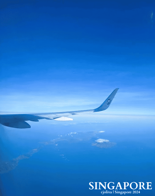 View from airplane window showing wing, ocean, islands, and scattered clouds en route to Singapore aboard Scoot Airlines.