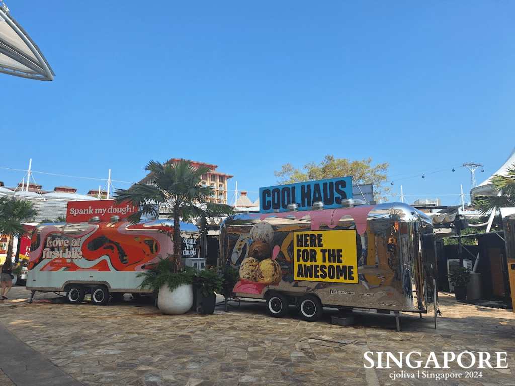 Colorful chrome food trucks, including Coolhaus, parked in an outdoor dining area at Sentosa, Singapore.