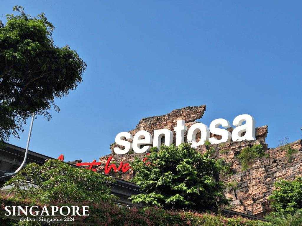 The white Sentosa signage mounted on a rocky cliffside against a clear blue sky in Singapore.