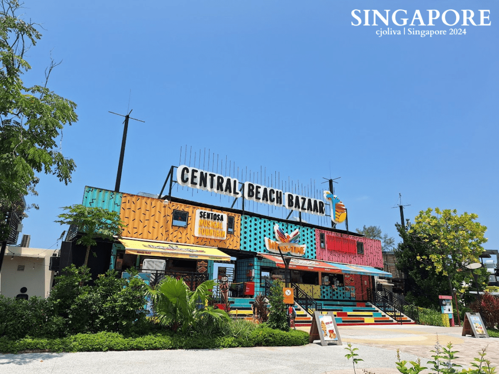 Colorful Central Beach Bazaar building in Sentosa, Singapore with turquoise, yellow, red, and orange panels, decorative patterns, and signage for Sentosa Musical Fountain.