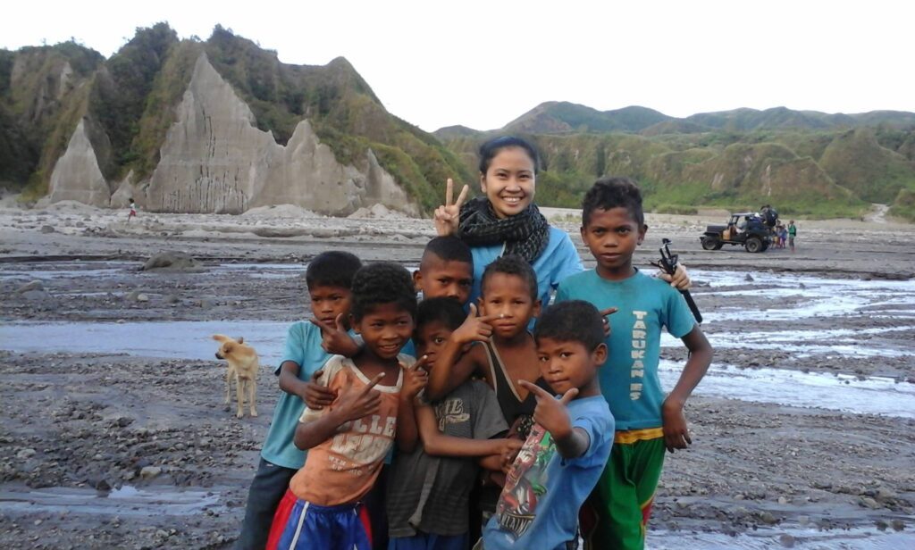 A woman tourist smiles and makes a peace sign while posing with local Aeta children in the lahar field near Mount Pinatubo, Philippines.