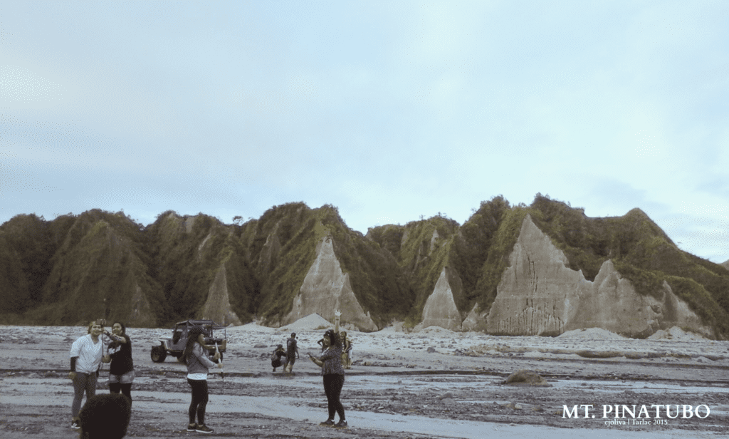 Tourists posing and taking photos on the lahar fields of Mt. Pinatubo with jagged volcanic peaks in the background.