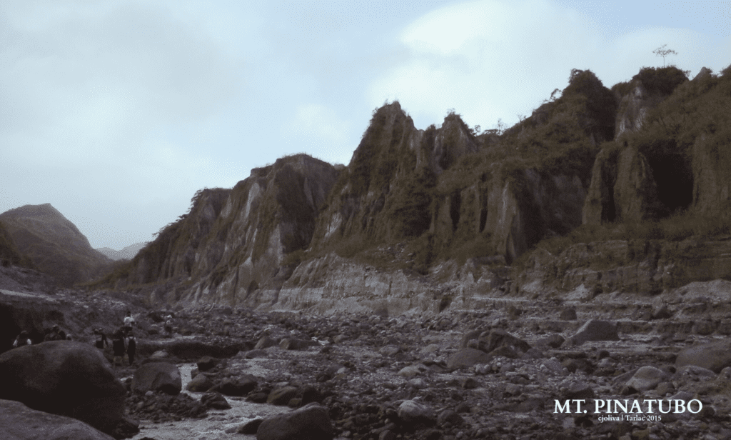 A wide view of the rocky riverbed and steep, greenery-covered volcanic cliffs on the trail to the Mt. Pinatubo crater.