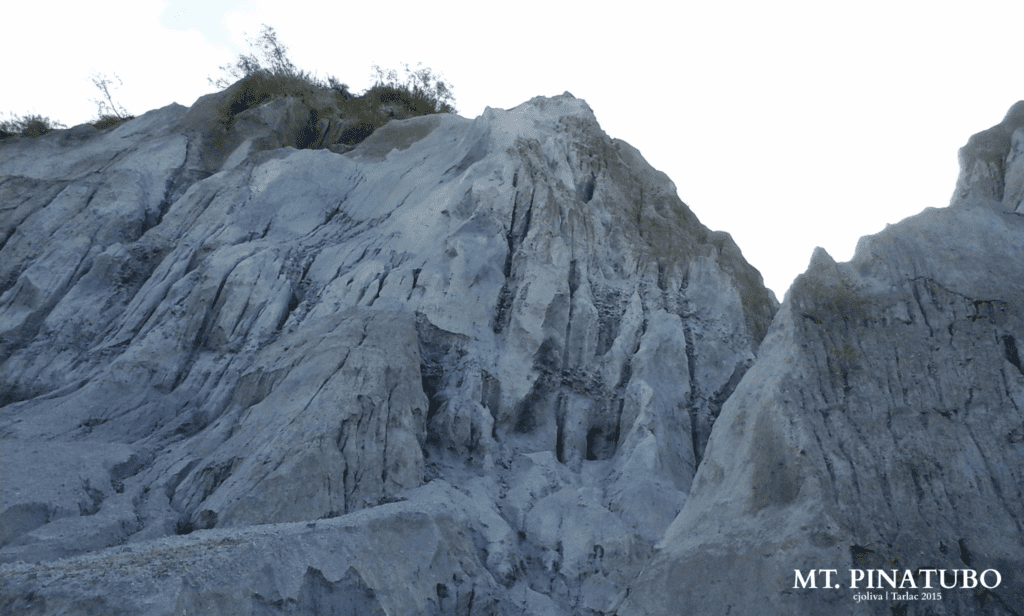 A close-up view of the towering, grey lahar and volcanic ash cliffs at Mount Pinatubo, showing deep erosion patterns.