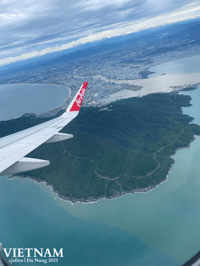 An aerial photograph from an AirAsia flight window showing the lush green Son Tra Peninsula, the coastline of Da Nang, and the Han River meeting the ocean.
