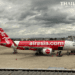 A side profile of a red and white AirAsia Airbus A320 airplane parked at the gate under a cloudy sky at Don Mueang International Airport, Bangkok.