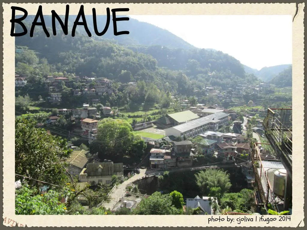 A high-angle view of Banaue town nestled in a lush green valley, showing local houses, a large school building, and winding mountain roads in Ifugao.