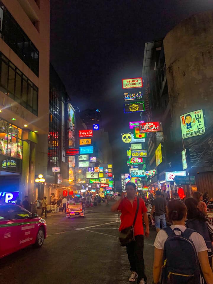 Busy street at night in Bangkok with colorful neon signs, people walking, and a pink taxi