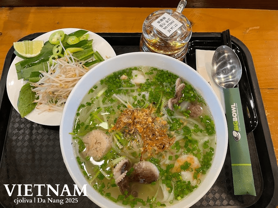 A steaming bowl of Vietnamese noodle soup with baby octopus, shrimp, and green onions, served with a side of bean sprouts, lime, and chili oil at Big Bowl, Da Nang.