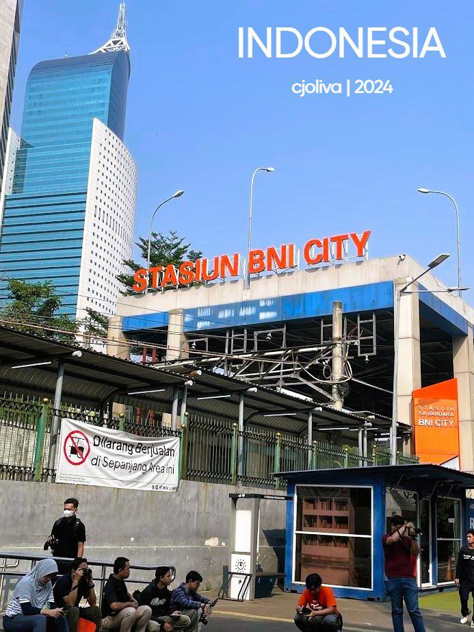 Exterior of Stasiun BNI City in Jakarta, Indonesia, with bold orange signage, a modern skyscraper backdrop, and people gathered near the entrance.