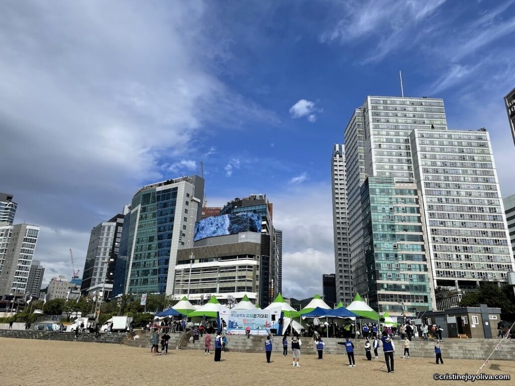 Busan beachside urban event with tents, people, and modern buildings