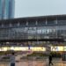 "Exterior of Busan Station with glass facade, multilingual signage, people walking with umbrellas on rainy day, and skyscrapers in background