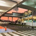 Soekarno–Hatta International Airport skybridge in Jakarta at sunset, with modern glass architecture, clean road markings, and a vivid orange-pink sky.
