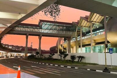 Soekarno–Hatta International Airport skybridge in Jakarta at sunset, with modern glass architecture, clean road markings, and a vivid orange-pink sky.