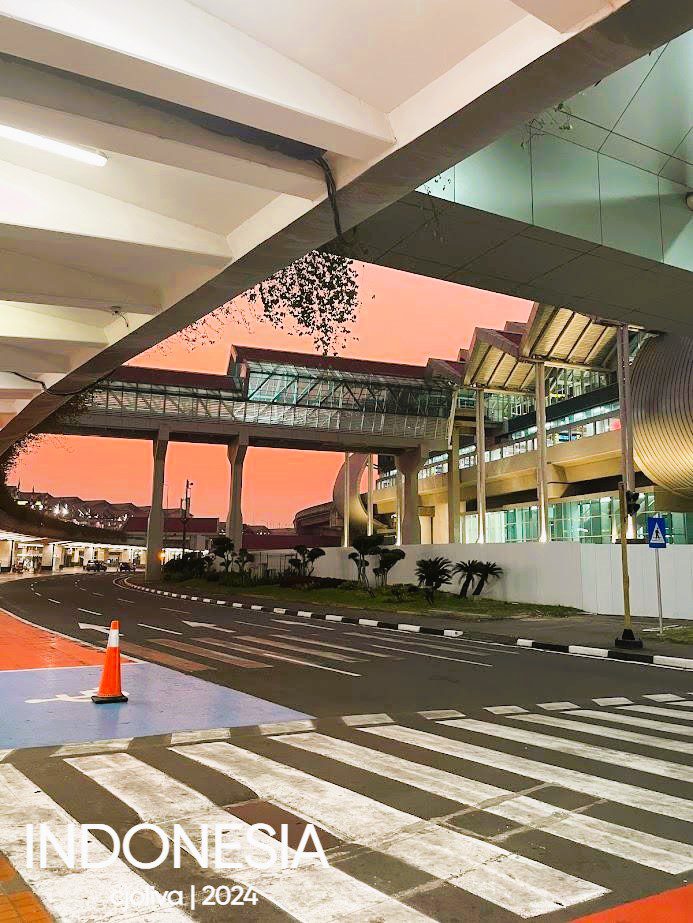 Soekarno–Hatta International Airport skybridge in Jakarta at sunset, with modern glass architecture, clean road markings, and a vivid orange-pink sky.