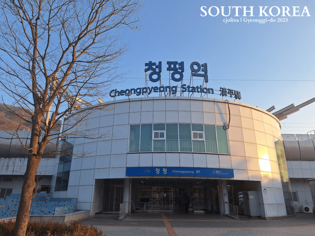 Exterior of Cheongpyeong Station in Gyeonggi-do, South Korea, with a modern curved facade, multilingual signage, and a leafless tree in the foreground.