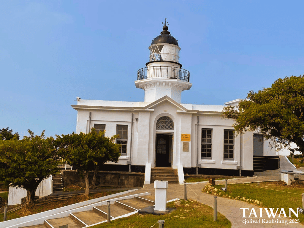 White lighthouse with black-domed lantern room and arched entrance surrounded by landscaped walkway in Kaohsiung, Taiwan
