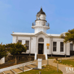White lighthouse with black-domed lantern room and arched entrance surrounded by landscaped walkway in Kaohsiung, Taiwan
