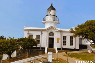 White lighthouse with black-domed lantern room and arched entrance surrounded by landscaped walkway in Kaohsiung, Taiwan