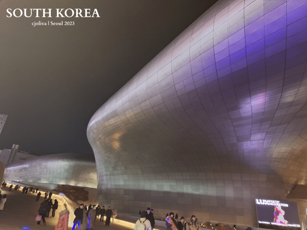 Dongdaemun Design Plaza in Seoul, South Korea at night with futuristic curved architecture illuminated in purple and blue lights.