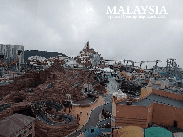 Amusement park in Genting Highlands, Malaysia, with roller coasters winding through artificial mountains, colorful structures, and a dramatic overcast sky.